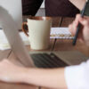 Business team collaborating at office desk with laptops, notebooks, and coffee cups during meeting
