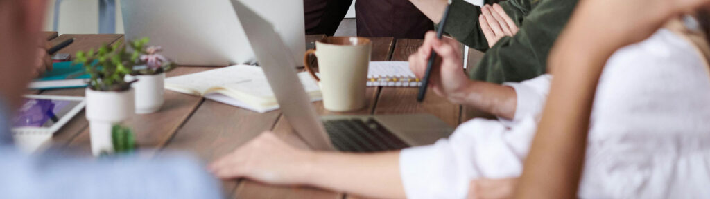 Business team collaborating at office desk with laptops, notebooks, and coffee cups during meeting