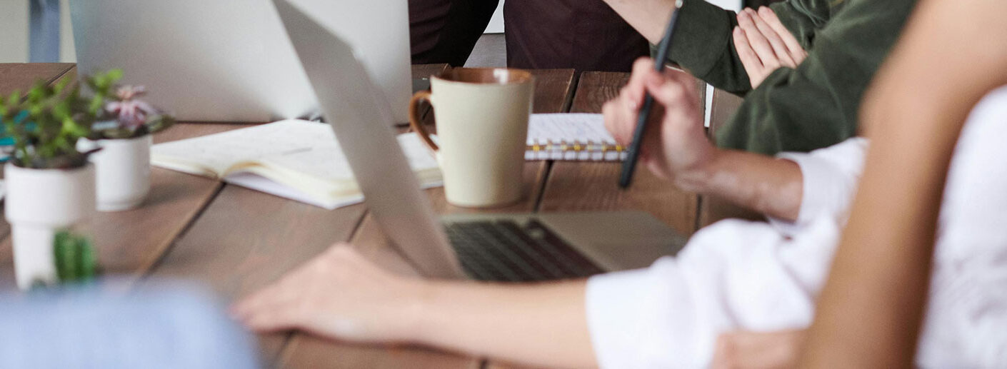 Business team collaborating at office desk with laptops, notebooks, and coffee cups during meeting