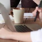 Business team collaborating at office desk with laptops, notebooks, and coffee cups during meeting
